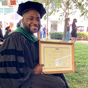 Utibe Essien, MD, MPH sitting while holding the 2021 Alumni Award at the Albert Einstein College of Medicine commencement ceremony